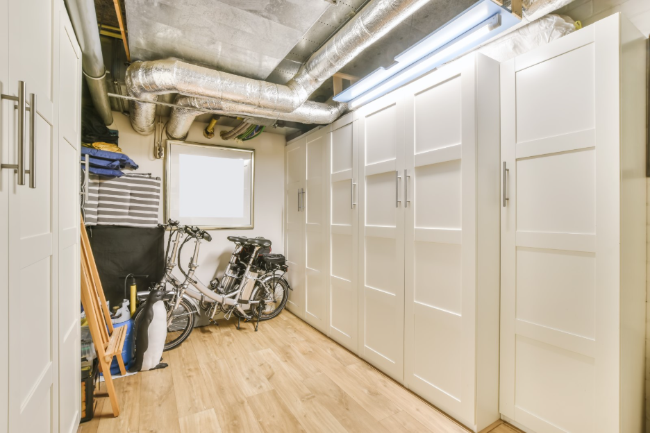 Finished basement storage area with built-in white cabinets, exposed HVAC ductwork, wood-look flooring, bicycles, and organized household items.